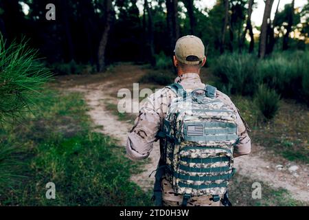 Back view of special force military soldier wearing camouflage uniform with cap and backpack standing in forest at sunset Stock Photo