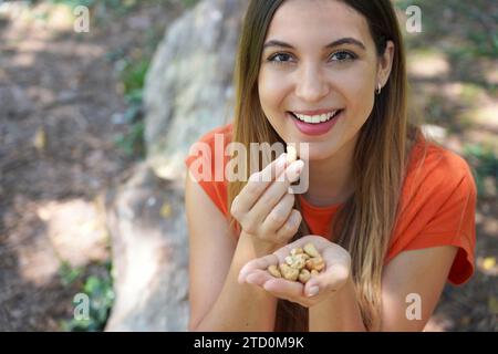 Beautiful healthy girl picking cashew nuts from her hand in the park. Looks st camera. Stock Photo