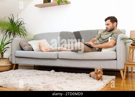 Man lying down on sofa at home and using his laptop. Working from home. Domestic lifestyle. Stock Photo
