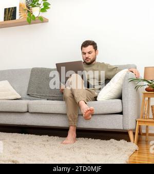 Man sitting on sofa at home and using laptop. Working from home. Home office. Stock Photo