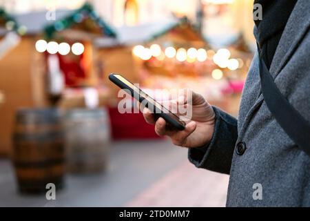 Mobile phone in hand of man in front of Christmas Fair. Stock Photo