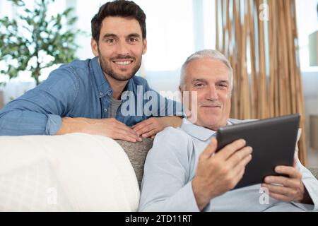son and elderly father sit on couch Stock Photo