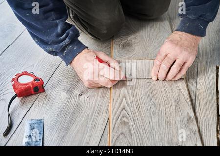 Close up of man construction worker with pencil in hand drawing line on laminate timber board. Male worker preparing laminate material for floor installation at home during renovation. Stock Photo