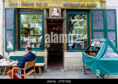 A person sits next to one of the entrances of the Shakespeare and Company bookshop. Antiquarian books. Parisian literature symbol. Stock Photo