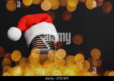 Christmas music. Microphone with Santa hat on black background, bokeh effect Stock Photo