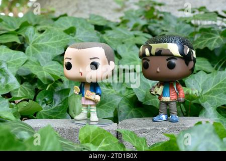 Funko Pop action figures of Eleven and Lucas from Netflix supernatural TV series Stranger Things. Green ivy plant leaves, abandoned garden, friends. Stock Photo