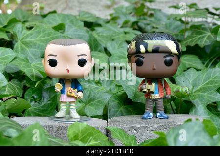 Funko Pop action figures of Eleven and Lucas from Netflix supernatural TV series Stranger Things. Green ivy plant leaves, abandoned garden, friends. Stock Photo