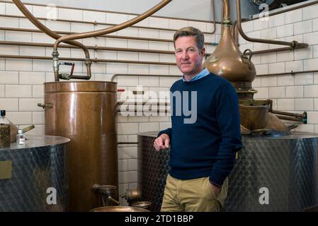 A male small business owner stands with his gin making equipment in an artisan distillery. Stock Photo