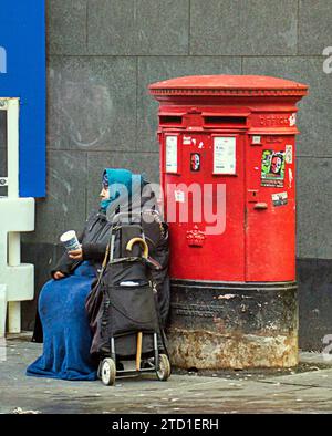 Glasgow, Scotland, UK. 15th December, 2023. UK Weather:  Cloudy  saw a miserable wet day  in the city centre. A refugee beffar commenderes a post box. Credit Gerard Ferry/Alamy Live News Stock Photo