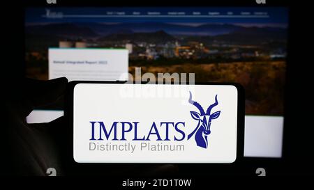 Person holding cellphone with logo of company Impala Platinum Holdings Limited (Implats) in front of business webpage. Focus on phone display. Stock Photo