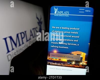 Person holding smartphone with webpage of company Impala Platinum Holdings Limited (Implats) in front of logo. Focus on center of phone display. Stock Photo