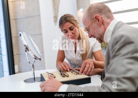 optician and customer smiling and looking at a selection of eyeglasses on a table Stock Photo