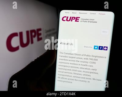 Person holding cellphone with webpage of trade union Canadian Union of Public Employees (CUPE) in front of logo. Focus on center of phone display. Stock Photo