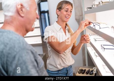 Optician assisting a senior customer with eyewear choice. smiling woman holding spectacles in optical store. Stock Photo