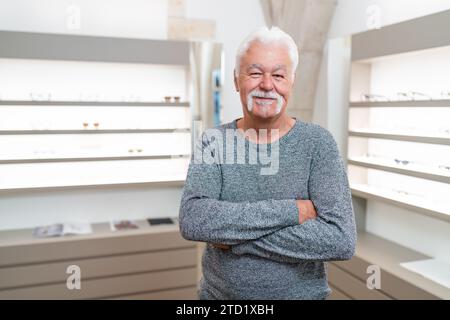 Senior customer with white hair smiling. He has his arms crossed in an eyewear store. Stock Photo