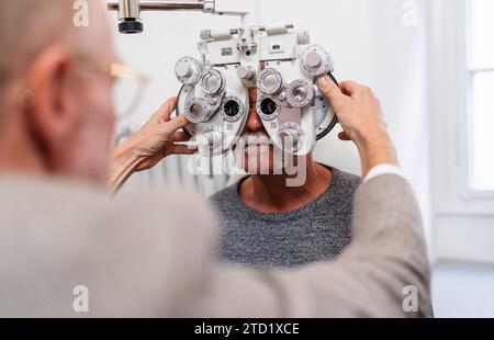 Optometrist adjusting phoropter for senior patient's vision test in clinic . Stock Photo