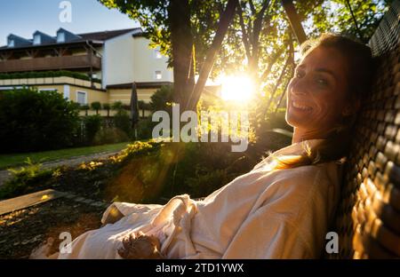 Smiling woman enjoying the morning sun on a wicker swing in a garden at sap wellness resort hotel Stock Photo