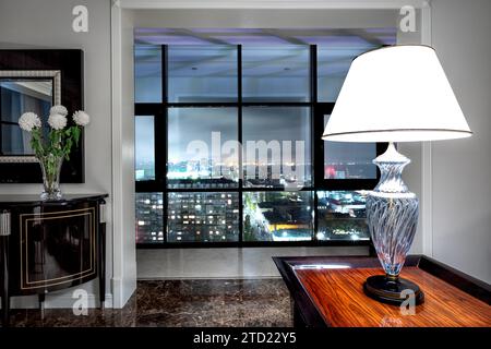 A floor lamp on a table in front of a panoramic window overlooking the night city. Stock Photo