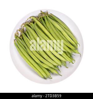 Fresh green beans in a white bowl. Young, unripe fruits of a cultivar of the common bean or also French bean, Phaseolus vulgaris. Close-up, isolated. Stock Photo
