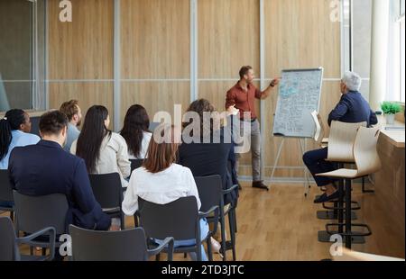 Professional business coach giving presentation for diverse audience in modern office Stock Photo