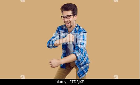 Happy male student in a plaid shirt and glasses dancing on a beige color background Stock Photo