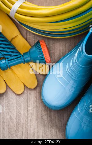 Hand spraying rubber hose with spray nozzle leather safety gloves and rubber boots on wooden board gardening concept Stock Photo