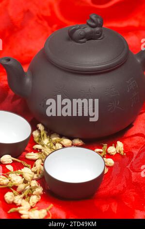 Jasmine tea dry flowers, pot and two cups, over red silk tablecloth, food photography Stock Photo
