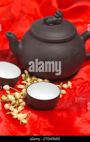Jasmine tea dry flowers, pot and two cups, over red silk tablecloth, food photography Stock Photo