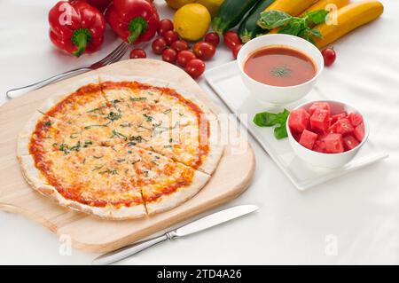 Italian original thin crust pizza Margherita with gazpacho soup and watermelon on side, and vegetables on background, food photography Stock Photo