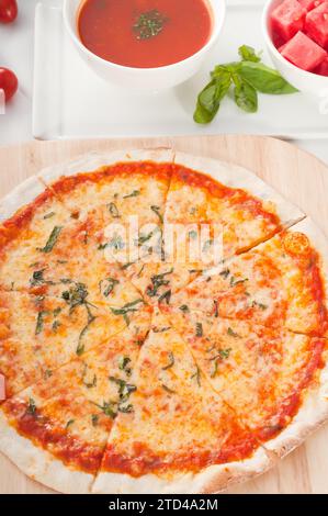 Italian original thin crust pizza Margherita with gazpacho soup and watermelon on side, and vegetables on background, food photography Stock Photo