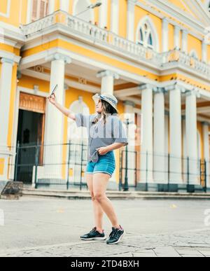 Beautiful tourist in hat taking selfie in the cathedral of Granada. Young travel woman taking a selfie in a public square Stock Photo