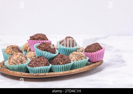A golden plate with dark rum balls in pastel-coloured paper cups, nut and chocolate sprinkles, copy space Stock Photo