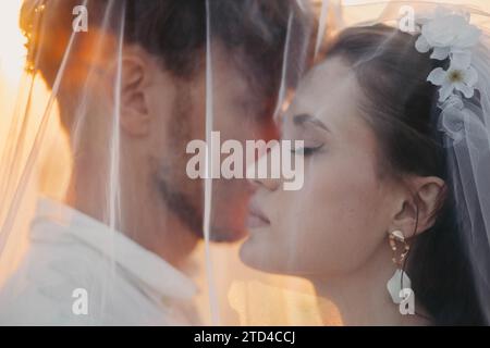 Beautiful young couple in love, newlyweds under a veil, love story at sunset Stock Photo