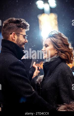 Young beautiful couple in love dancing in the city under snowfall on valentine's day Stock Photo