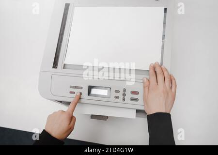 The hands of a young woman is placing a piece of paper on a flatbed scanner in preparation for copying it Stock Photo