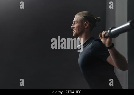 Young handsome crossfit athlete doing exercise with barbell in gym. Happy smiling man warming up and preparing before training. Crossfit, sport, bodybuilding and healthy lifestyle concept. Copy space Stock Photo