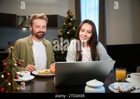 Woman and man having festive Christmas breakfast using laptop Stock Photo