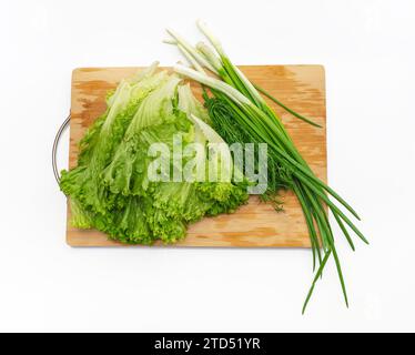 Green salad, green onions and bunch of dill on wooden cutting board. Side view. Fragrant greens. Stock Photo