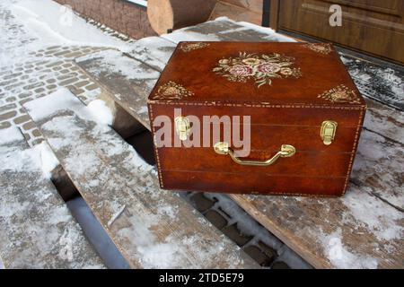 Old wooden antique box on wooden open porch. Wooden antique patterned patterned suitcase for storing clothes. Stock Photo