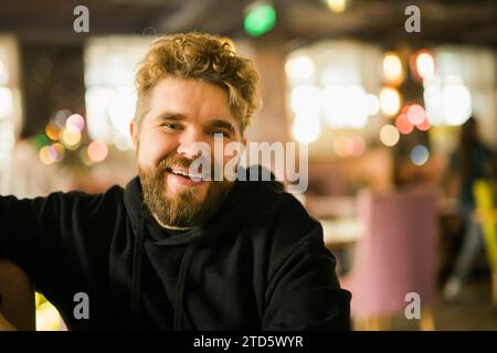 Bearded guy programmer or an entrepreneur in glasses in a stylish cafe looks at the camera and smiles copy space and empty space for advertising Stock Photo