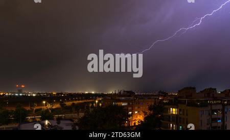 Stormy sky raining with a huge lightning bolt drawing a diagonal in the sky on the outskirts of a city over buildings. Weather concept Stock Photo