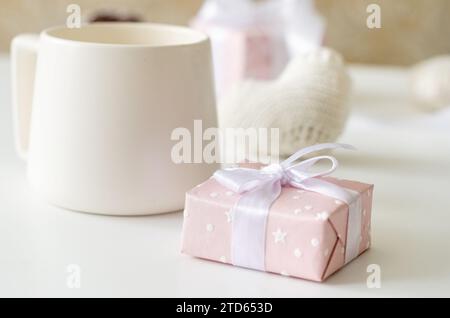 Pink gift box with a bow and a cup of tea on a white background. Winter holidays concept. Copy space. Stock Photo