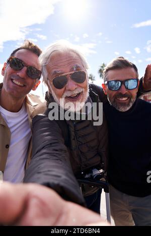 Cheerful group of middle-aged Caucasian men wearing sunglasses taking a selfie with a cell phone. Stock Photo