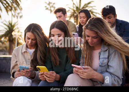 Diverse group of university friends sitting on street staircase, serious people using smart phones Stock Photo