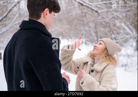 A young couple walks in the winter in the forest. Deaf Guy and a girl communicate using gestures outdoors. Stock Photo