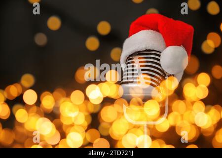 Christmas music. Microphone with Santa hat on black background, bokeh effect Stock Photo