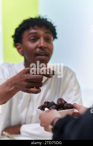 African American Muslim man delicately takes dates to break his fast during the Ramadan month, seated at the family dinner table, embodying a scene of Stock Photo