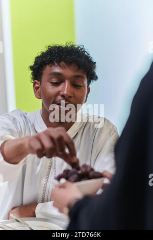 African American Muslim man delicately takes dates to break his fast during the Ramadan month, seated at the family dinner table, embodying a scene of Stock Photo