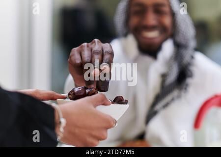 African American Muslim man delicately takes dates to break his fast during the Ramadan month, seated at the family dinner table, embodying a scene of Stock Photo