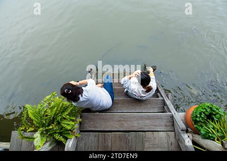 Nonthaburi, Thailand - October 29, 2023 : Top view of people sitting and feeding fish on stairs at the pier in Bang Yai District Nonthaburi Province, Stock Photo